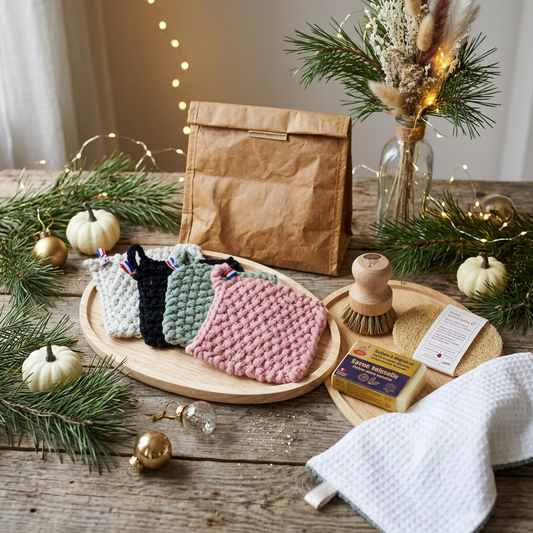 Coffret cadeau Noël Cuisine au naturel : tawashis tricotés main, kit vaisselle avec savon solide et brosse en bois, lavette microfibre nid d'abeille et sac à sandwich isotherme en kraft sur une table en bois brut avec décorations de Noël